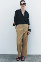 Pantalón color beige de corte ancho, con tiro medio, trabillas en la cintura y raya planchada.