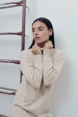 Vestido corto color beige de tejido de punto, con cuello alto tipo polera y mangas largas. Corte recto y terminaciones acanaladas en puños, cuello y ruedo.