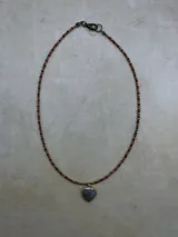 Collar de múltiples hebras con cuentas pequeñas de tonos tierra, rojo y azul, y dijes colgantes en forma de corazón con piedras semipreciosas engarzadas en metal dorado.