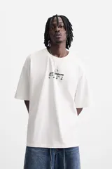 Camiseta blanca de corte relajado, cuello redondo y manga corta. Presenta un estampado de gráficos y textos combinados a contraste en la parte delantera y trasera.