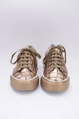 Zapatillas bajas color marrón con textura simil cuero de cocodrilo, cordones al tono y suela de goma blanca con detalle marrón.