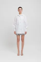 Camisa blanca de popelina con doble tapeta, broches metálicos a presión y corte ligeramente oversize.