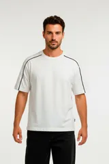 Remera de algodón color gris oscuro con efecto lavado, corte holgado y cuello redondo. Presenta un ribete blanco fino que recorre la costura del hombro y el borde de la manga.