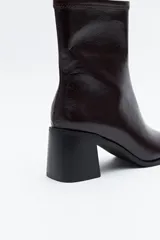 Bota corta de caña elástica, color negro con acabado charolado. Presenta puntera cuadrada y taco medio geométrico y ancho.