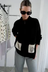 Campera tejida con textura vanizada a rayas horizontales en blanco y negro, con cierre frontal y flecos negros en forma de V en el pecho.