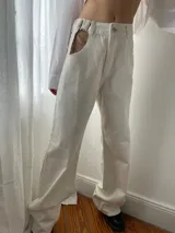 Pantalón de jean blanco de corte wide leg, con botón y cierre metálico color níquel. Presenta un recorte en la cadera con detalle de cadena metálica.
