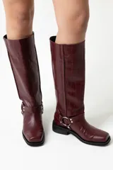 Botas de cuero color bordó con textura croco, caña alta con correa decorativa con argolla metálica y taco bajo.