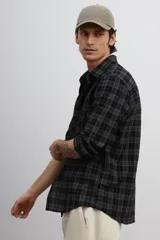 Camisa de popelina de algodón texturizado a cuadros negros y grises, de corte holgado, con cuello inglés, tapeta lisa, canesú con pliegue de caja en la espalda, mangas largas con abertura y cierre ajustable de botón en los puños, y bajo levemente redondeado.