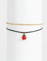 Set de dos chokers: uno de cadena dorada y otro de cordón negro con dije esmaltado de vaquita de San Antonio.