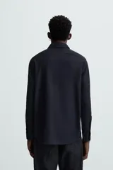 Camisa negra de manga larga con cuello italiano y cierre frontal de botonadura. Presenta un tejido con estructura de fácil cuidado.