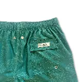 Short de baño verde con estampado de hojas en color crema, cintura elástica con cordón ajustable y logo de la marca en la pierna izquierda.