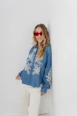 Camisa de denim azul con bordados en color crudo, de corte relaxed, manga larga y botones frontales.