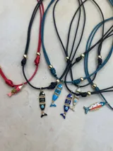 Collar con cordón ajustable de color y dije de pez esmaltado con detalles de piedras de colores.