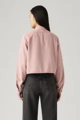 Camisa color rosa pálido, de corte cropped, con cuello camisero, cierre frontal con botones, mangas largas abullonadas con puños elásticos, dos bolsillos de parche en el pecho y canesú en la espalda.