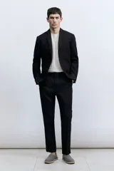 Blazer negro de lino liviano con solapas de muesca finas y ojal decorativo. Modelo de botonadura sencilla con bolsillo superior, bolsillos delanteros con solapa y dos bolsillos en el interior. Cierre de dos botones, botones decorativos en los puños y abertura doble atrás. Corte ajustado que realza el contorno del cuerpo creando una silueta entallada. Forrado.