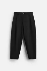Pantalón negro de corte amplio tipo balloon fit, con cintura con pliegues frontales, bolsillos delanteros y traseros de plastrón. Cierre frontal con cremallera y botón.