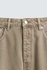 Pantalón de denim color beige, corte relaxed fit, con bolsillos laterales tipo cargo con solapa y cierre de botón. Cierre frontal con botón y cremallera.