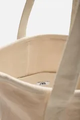 Bolso tipo shopper color crudo, fabricado en tejido de algodón. Tiene doble asa de hombro y un bolsillo interior plano.