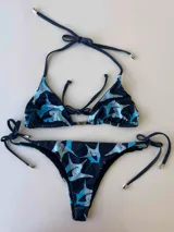 Conjunto de bikini con estampado de figuras abstractas en tonos azul y celeste. El corpiño es de triángulo con tiras finas para atar en el cuello y la espalda. La bombacha es de corte clásico con tiras laterales ajustables.