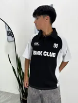 Chomba deportiva bicolor, negra en el torso y blanca en las mangas y laterales. Tiene cuello polo negro con botones y estampado frontal con el texto "BNK CLUB" y el número "00".