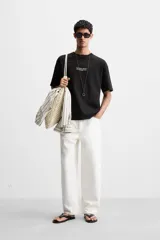 Camiseta negra de corte holgado con cuello redondo y mangas cortas. Estampado frontal con la frase "Unfolding Dreams" en letras blancas.