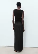 Falda larga negra de lino, con forro de algodón, cintura elástica, tiro medio, diseño lápiz, abertura en la parte posterior y cierre de cremallera lateral.