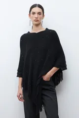 Capa tejida color negro, con cuello redondo, diseño de punto y detalles de lentejuelas. Presenta flecos en el dobladillo.