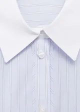 Camisa celeste a rayas verticales, de corte recto y manga larga con puños abotonados en blanco. Presenta cuello camisero blanco, cierre frontal con botones y un bolsillo de parche en el pecho.