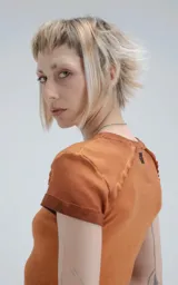 Remera de manga corta y cuello redondo, confeccionada en tejido ribb 100% algodón, de calce ajustado al cuerpo y largo a la cadera. El color es un marrón oscuro con efecto desgastado o teñido. Presenta costuras externas visibles en los hombros y laterales.