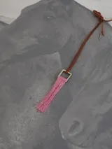 Collar con cordón marrón, dije cuadrado plateado y flecos rosas.