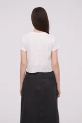 Remera blanca con calados formando flores, de corte crop y mangas cortas con dobladillo.
