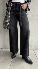 Pantalón de jean negro de corte recto, con tachas plateadas y cinturón fino con hebilla metálica.