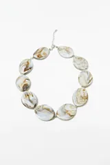 Collar de cuentas grandes ovaladas de color crudo con efecto veteado en tonos marrones, engarzadas con hilo metálico plateado y cierre de mosquetón con cadena de alargue.