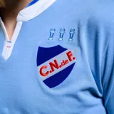 Camiseta de fútbol Umbro del Club Nacional de Football, modelo Away 3 temporada 2024. Diseño celeste con cuello polo blanco y detalles en rojo. Incluye logo de Umbro, escudo del club y sponsor Antel en el frente.