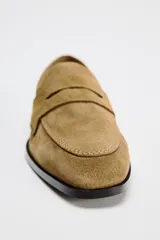 Zapato plano tipo mocasín color marrón claro, confeccionado en piel de serraje. Tiene copete subido, antifaz y punta redonda.