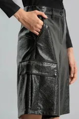 Bermuda de símil cuero brillante color negro, de calce relajado, tiro medio y largo a la rodilla. Presenta bolsillos cargo laterales, bolsillos delanteros, pinzas traseras, presillas y broche delantero.
