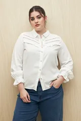 Camisa blanca de manga larga confeccionada en viscosa ligera, con cuello camisero, cierre frontal con botones y puños elastizados. Presenta detalles calados en la parte superior y pequeños volados.