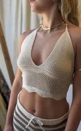 Conjunto de dos piezas tejido a crochet, compuesto por un top halter y un pantalón acampanado. El tejido es calado con rayas horizontales en tonos beige claro y marrón.