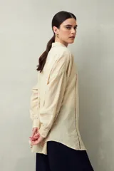 Camisa blanca de lino con botones de nácar, corte recto, cuello clásico y mangas largas con puños abotonados. Presenta detalles de calados tipo vainillas en el frente y las mangas.
