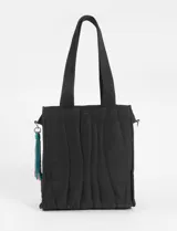 Bolso tipo shopper color negro, con diseño acolchado y pespuntes ondulados. Posee asas de hombro y un accesorio colgante tipo borla con detalles en turquesa, verde y rosado.