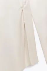 Camisa color blanco hueso de corte holgado, con cuello solapa, manga larga y cierre frontal con botones. Presenta detalle de botones en la cintura.