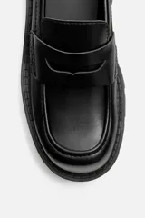 Mocasín negro de cuero con antifaz, horma cuadrada y suela track con volumen.