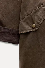 Trench color verde oscuro con cuello solapa combinado en pana marrón y manga larga. Detalle de acabados con trabillas y pinza en espalda. Bolsillos delanteros con solapa y botón a presión. Tejido encerado efecto lavado. Cierre frontal con botones a presión.