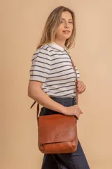 Bandolera de hombro color gris claro, con solapa frontal y correa ajustable. Presenta un diseño simple y práctico, ideal para uso diario.