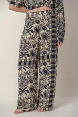Pantalón de dama con estampado de hojas, flores y soles en tonos beige y negro.