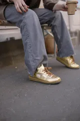 Championes deportivos de cuero y gamuza color dorado metalizado y marrón. Suela de caucho color crema con línea roja. Cordones color crema.