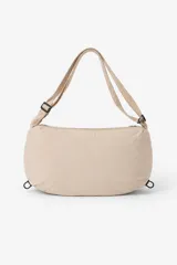 Bandolera color beige, con forma rectangular y extremos redondeados. Tiene una correa ajustable con hebilla negra y cierre de cremallera en la parte superior.