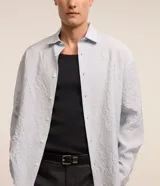 Camisa celeste de viscosa y poliéster con textura arrugada, cuello tradicional, manga larga y abotonadura frontal completa.