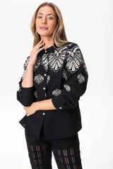 Camisa negra de lino con bordados florales blancos, de corte clásico, cuello camisero y mangas largas con puños abotonados.