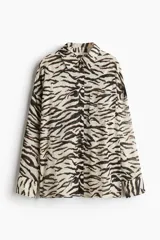 Camisa de manga larga con estampado de cebra en tonos blanco y negro. Tiene cuello clásico, cierre frontal con botones y un bolsillo de parche en el pecho.